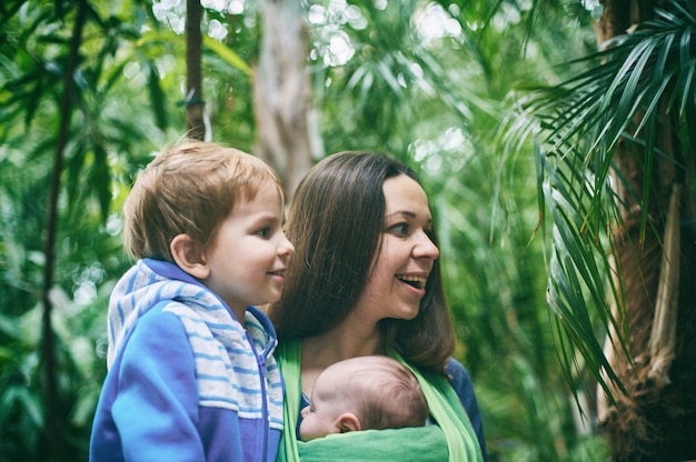 Una joven madre con un bebé en una honda y un niño pequeño está caminando en la selva