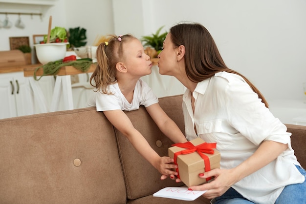Una joven madre besa a su hija y le agradece el regalo y la tarjeta