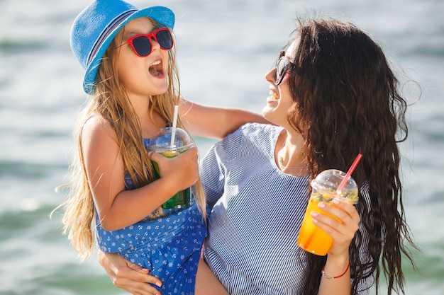 Joven madre bonita y su pequeña hija en la playa divirtiéndose