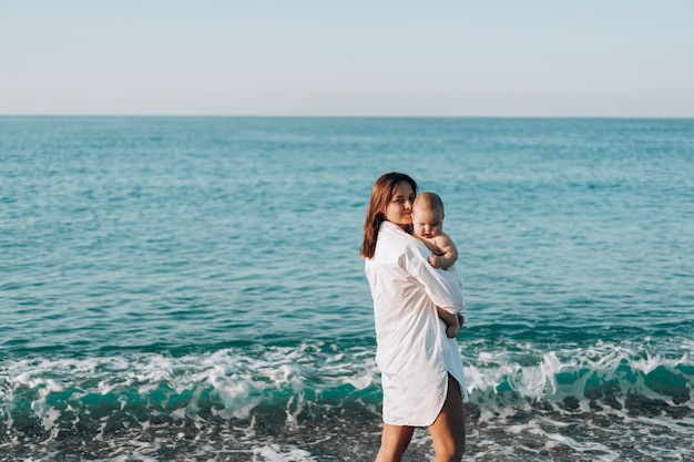 Una joven madre camina por la playa con un niño pequeño en pañales.