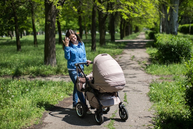 Joven madre caminando y empujando un cochecito en el parque