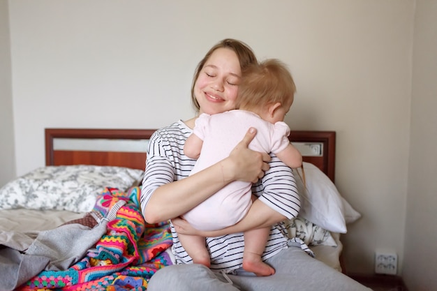 Joven madre caucásica feliz su pequeño bebé lindo y sonriente con los ojos cerrados