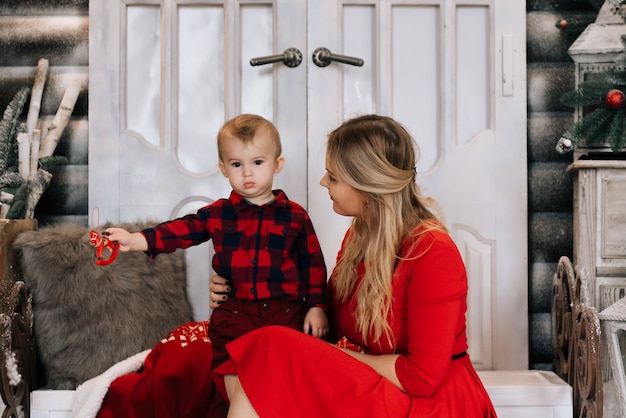 Joven madre caucásica con pequeño hijo cerca de árbol de Navidad. Concepto de celebrar las vacaciones de invierno y jugar con el bebé.