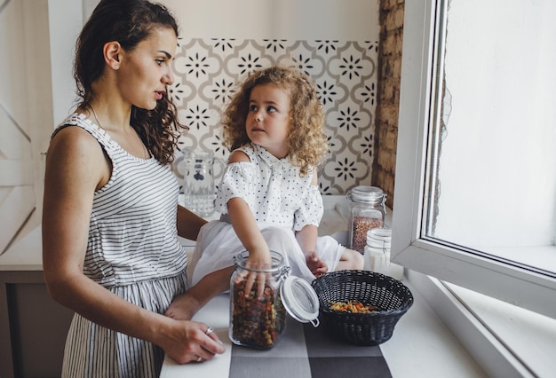 Una joven madre cocina pasta en la cocina con su pequeña hija. cocción conjunta