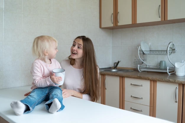 Joven madre y comunicación de niña linda en la mañana en la cocina.