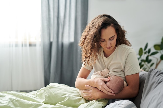 Joven madre cuidadosa amamantando a su lindo bebé mientras lo sostiene en las manos