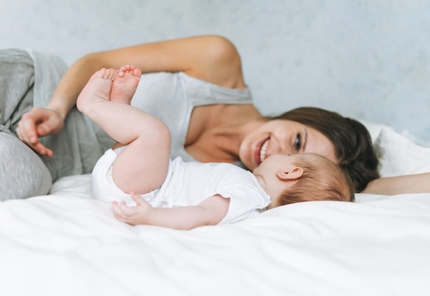 Joven madre divirtiéndose con linda niña en la cama con sábanas blancas tonos naturales amor emoción