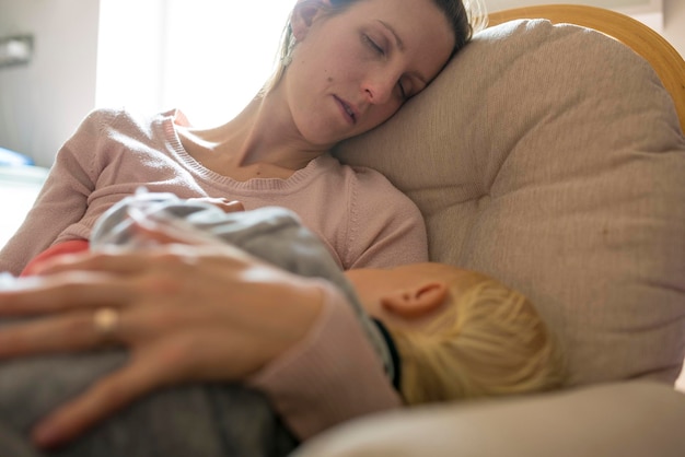 Joven madre durmiendo la siesta en una mecedora con un bebé durmiendo en su regazo