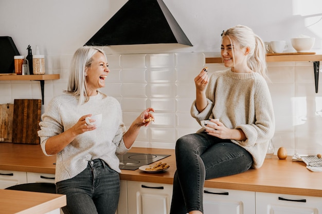 Joven madre e hija adolescente riendo y hablando en la cocina