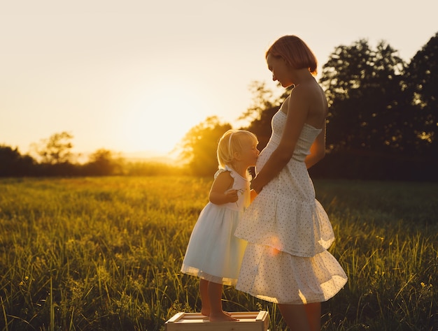 Joven madre e hija embarazadas en vestido en la naturaleza al aire libre Mujer embarazada y niño en la pradera