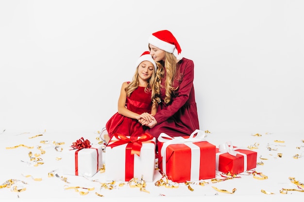 Joven madre e hija con gorros de Santa divirtiéndose con regalos de Navidad