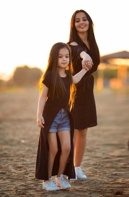 Joven madre e hija jugando y caminando en la playa de arena