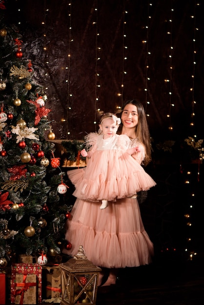 Una joven madre e hija con vestidos a juego decoran el árbol de Navidad con bolas nuevas