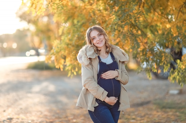 Joven madre embarazada camina en otoño en el parque con árboles amarillos