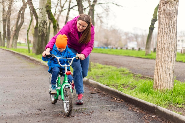 Una joven madre le enseña a su hijo a montar en bicicleta por primera vez en el parque