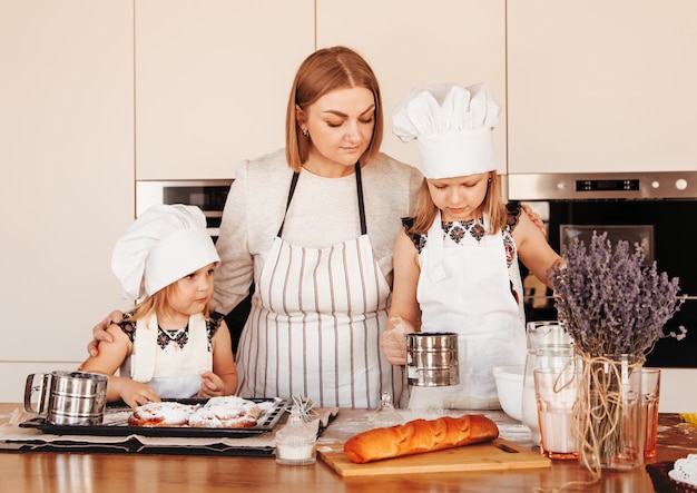 Una joven madre enseña a sus hijas a cocinar en la cocina. Los bollos se hornean juntos