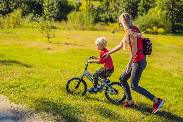 Joven madre enseñando a su hijo a andar en bicicleta en el parque.