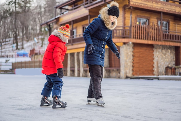 Joven madre enseñando a su pequeño hijo a patinar sobre hielo en la pista de patinaje al aire libre La familia disfruta del invierno en la pista de hielo al aire libre