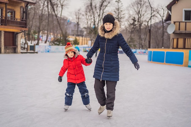 Joven madre enseñando a su pequeño hijo a patinar sobre hielo en la pista de patinaje al aire libre La familia disfruta del invierno en la pista de hielo al aire libre