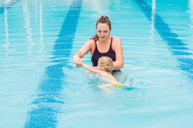 Joven madre enseñar a su pequeño hijo a nadar en una piscina