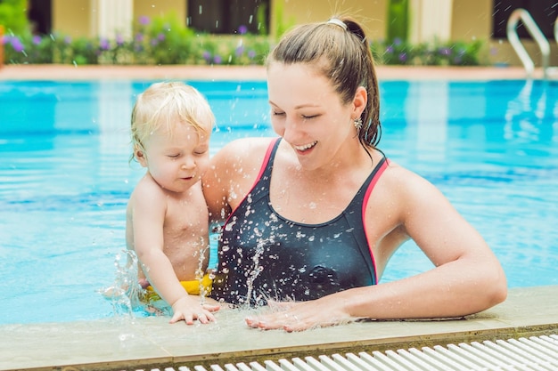 Joven madre enseñar a su pequeño hijo a nadar en una piscina