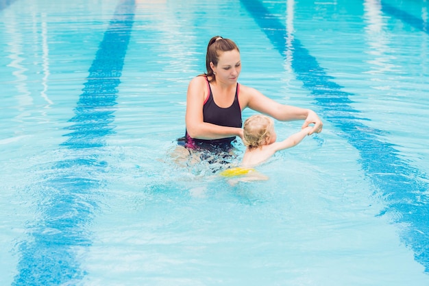 Joven madre enseñar a su pequeño hijo a nadar en una piscina