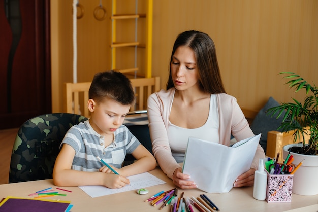 Una joven madre está haciendo la tarea con su hijo en casa. Padres y entrenamiento