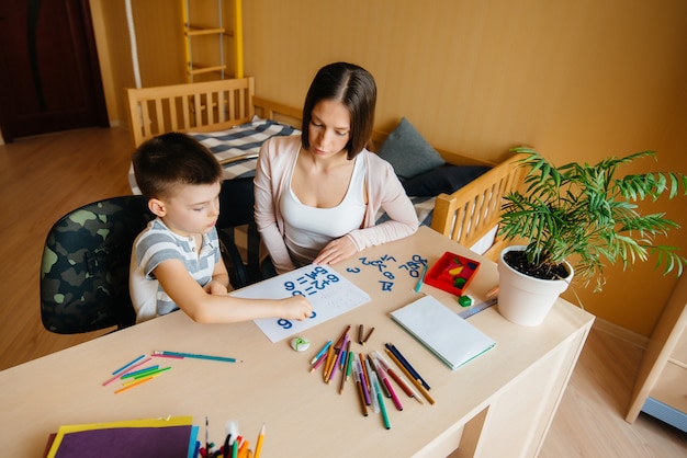 Una joven madre está haciendo la tarea con su hijo en casa. Padres y entrenamiento