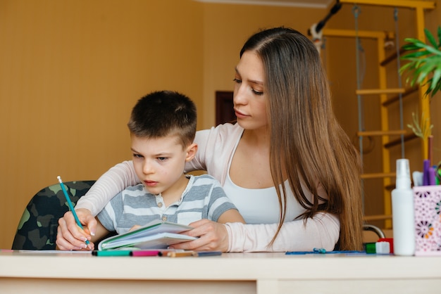 Una joven madre está haciendo la tarea con su hijo en casa. Padres y entrenamiento