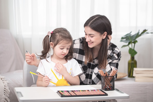 La joven madre está haciendo la tarea con su pequeña hija linda. Concepto de educación y educación en el hogar.