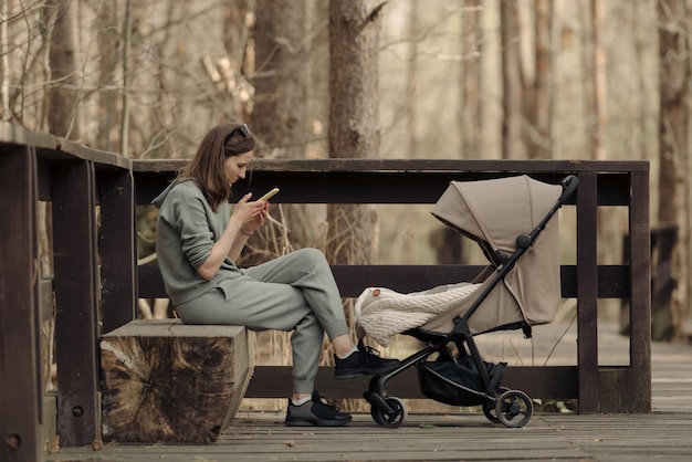La joven madre está trabajando con su teléfono celular mientras su hijo pequeño duerme en el cochecito de bebé La madre con su hijo en el parque para tomar aire fresco