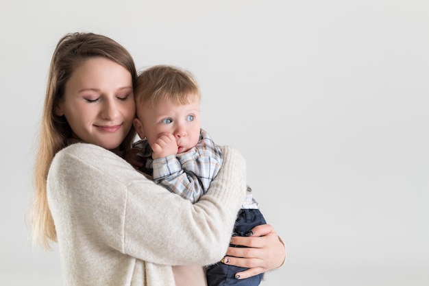 Joven madre feliz con los ojos cerrados sosteniendo al bebé en abrazos sobre fondo blanco.