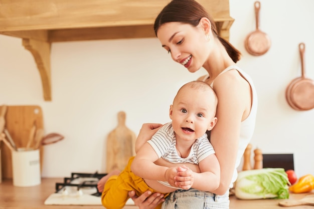 Foto una joven madre feliz sostiene a su pequeño hijo en brazos en la cocina