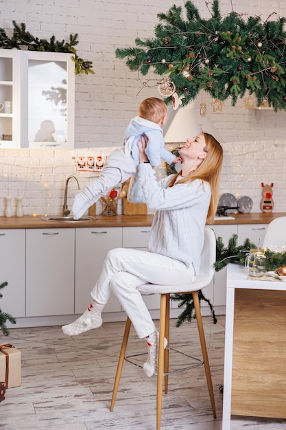 Una joven madre feliz con su hijo en brazos da la bienvenida al nuevo año Una mujer con un niño en el fondo de la cocina de Año Nuevo en casa