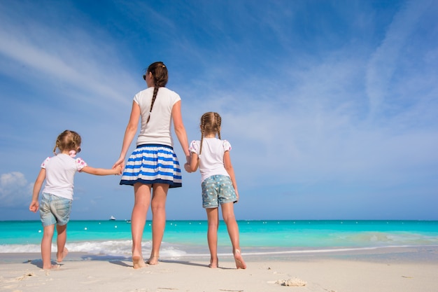 Joven madre feliz y sus adorables hijas divirtiéndose en la exótica playa en día soleado