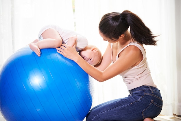 Joven madre haciendo ejercicios en la pelota de fitness con su lindo bebé niño