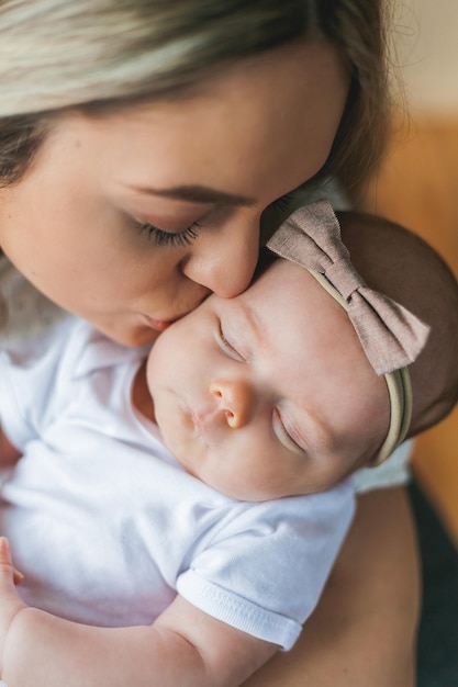 Joven madre hermosa con ojos azules sostiene a su pequeña hija recién nacida en sus brazos