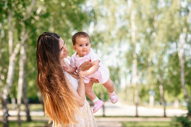 Una joven madre hermosa con una pequeña hija en las manos caminando en el parque.