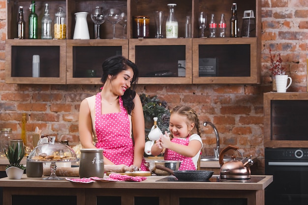 Joven madre hermosa y su pequeña hija cocinando juntos en la cocina