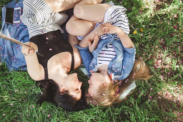 Joven madre hermosa y su pequeña hija haciendo selfie en teléfono móvil. Mamá y su bebé al aire libre divirtiéndose en el parque. Chicas haciendo fotos en celular y sonriendo