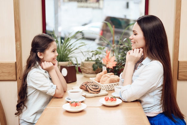 Foto joven madre con hija comiendo pasteles en la cafetería.