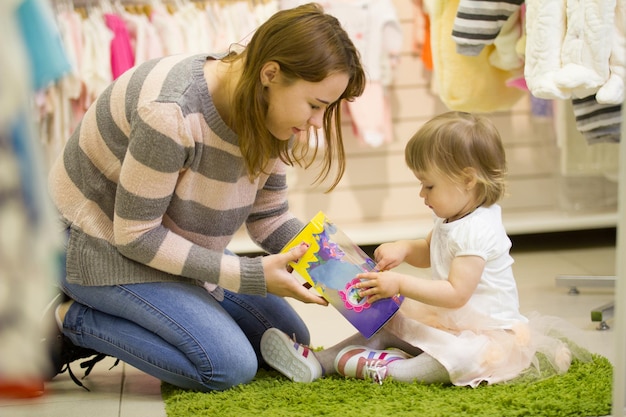 Joven madre con hija jugando con juguetes en la tienda para niños