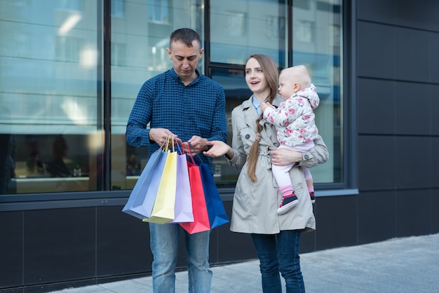 Joven madre con hija pequeña en los brazos. Padre con bolsas de compras en la mano. Familia de compras. Centro comercial