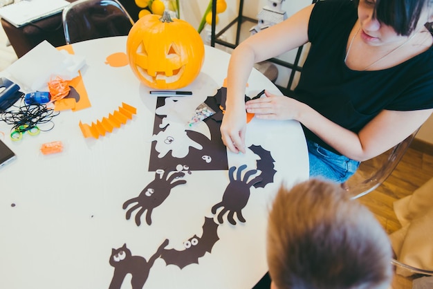 Joven madre con un hijo pequeño haciendo arañas artesanales para las vacaciones de halloween