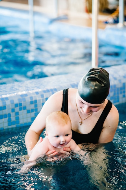 Joven madre, instructor de natación y niña feliz en la piscina. Enseña a los bebés a nadar. Disfruta el primer día de natación en el agua. Mamá sostiene al niño preparándose para bucear. haciendo ejercicios.