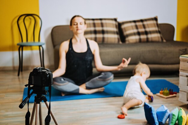 Joven madre instructora de fitness entrenador personal graba video cerca de la cámara en casa con su hija