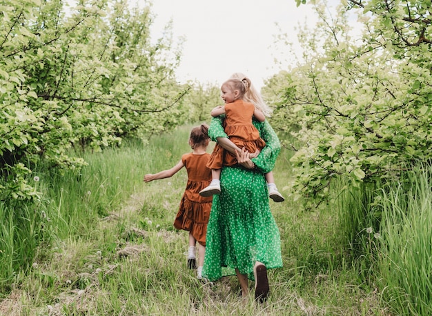 Una joven madre juega con dos hijas pequeñas en el jardín de primavera. niños felices y mamá