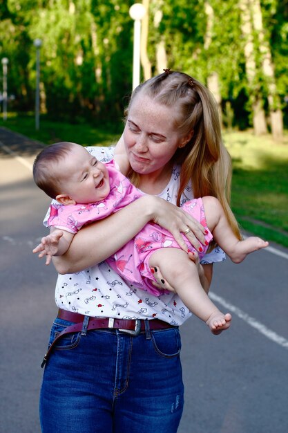 Joven madre jugando y riendo bebé en parque verde.