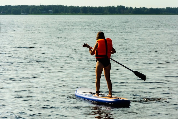 Una joven madre nada en una tabla de remo de pie Tabla de SUP Deportes acuáticos