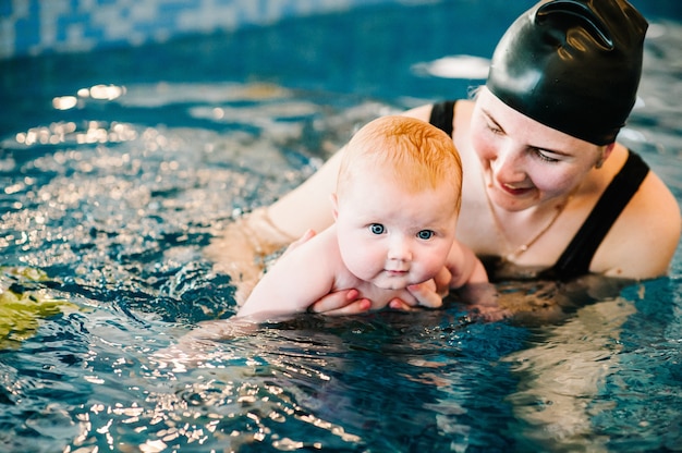 Joven madre, niña feliz en la piscina. Enseña a los bebés a nadar. Disfruta el primer día de natación en el agua. Mamá sostiene al niño preparándose para bucear. haciendo ejercicios. mano que lleva al niño en el agua